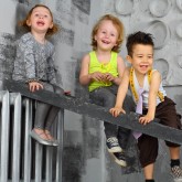 Three happy children sitting on the stairs near the gray wall