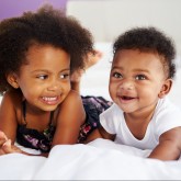 Sister With Baby Brother Lying On Parent's Bed